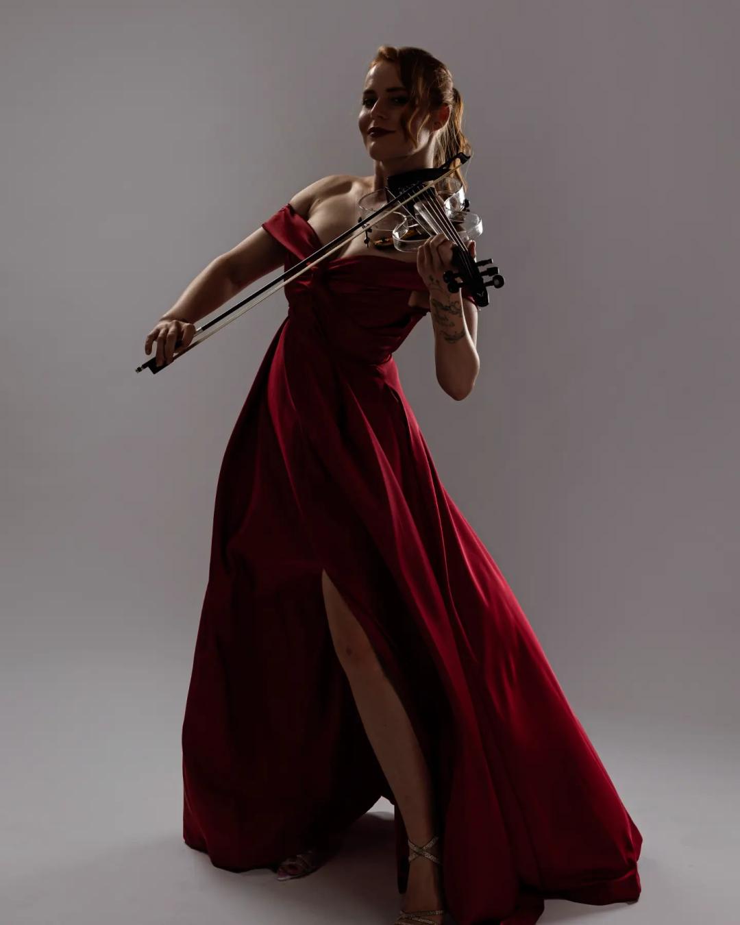 A woman in a beautiful red dress pretends to plays violin